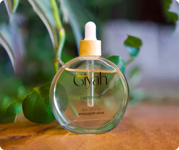Giyah castor oil dropper bottle on wooden table with green plants in background