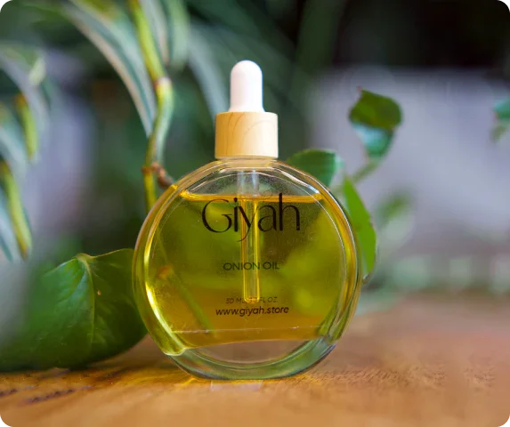 Giyah onion oil bottle with dropper on wooden surface, green leaves blurred in background